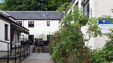 The entrance to a care home building, with white painted walls and some greenery surrounding it