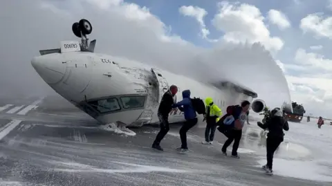 Passengers leave an upside down plane after it crashed on landing at Toronto Pearson International Airport in Mississauga, Ontario.