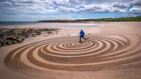 Artist Sean Corcoran, from Waterford, Ireland, creates a piece of sand art on the beach at Tyninghame, East Lothian, during the European Land Art Festival in Scotland. 4 July 2022.