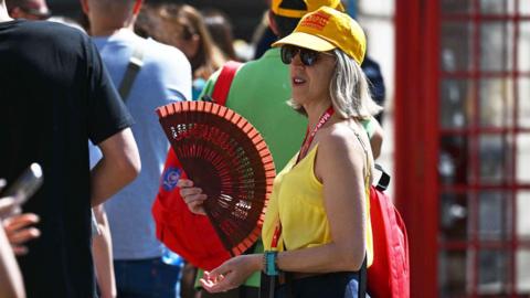A woman wearing a yellow top and holding a red fan