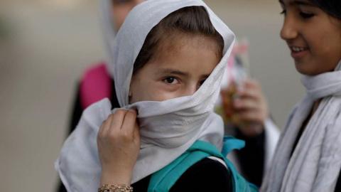 A girl wearing a white headscarf looks into the camera, accompanied by two other girls