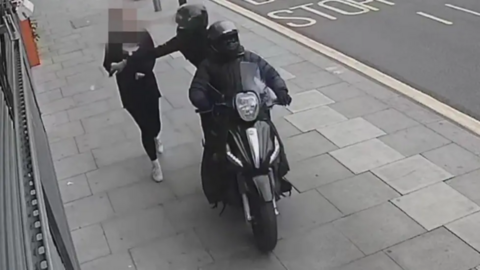A person on a moped snatching a phone out of the hands of a member of the public