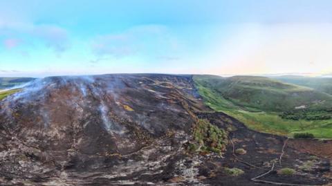 A wide-angle lens view of a moorland hill with large areas of burnt grass