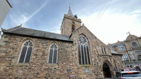 A picture of the town church in Guernsey. It is a brick design with taxis parked out the front of it.