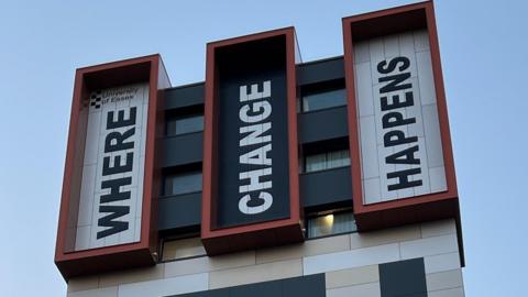 Large lettering at the top of a building that reads "Where change happens". Each of the three words is in a separate section of the facade, with the words written out vertically, starting with the first letter on its side at the bottom.