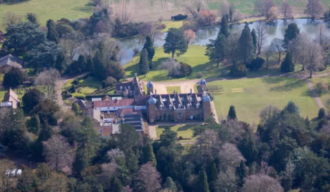 Wide aerial shot shows the grand estate of Althorp, with a large angular house and backed by a meandering river and forest