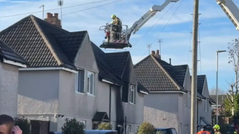 A firefighter on a cherry picker next to a blackened house