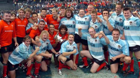 Wales players, some in red Wales shirts and some in blue and white Argentina jerseys, pose together on the pitch on the 2004 tour of Argentina.