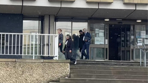 Four people walking from a court building. Three of their faces are blurred.
