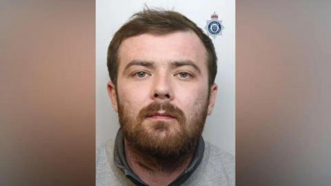 A mugshot of Sean Garner, who has a brown beard and is wearing a grey sweatshirt. 