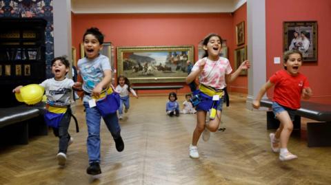 A group of children running through an art gallery smiling
