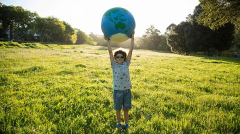 Child holding up planet Earth ball in a park