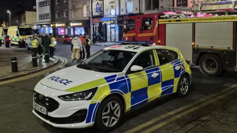 Emergency vehicles including a police car and a fire engine close to the scene of the incident.