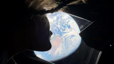  NASA astronaut and Artemis II mission specialist Christina Koch peers out of one of the Orion spacecraft's main cabin windows, looking back at Earth