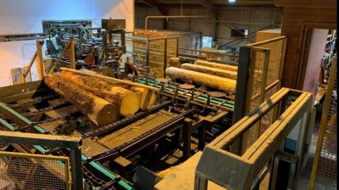 Photograph issued by the Health and Safety Executive of a machine used in the sawmilling trade. The large machine has several logs placed on it.