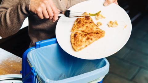 A woman throwing leftover pizza in to a bin