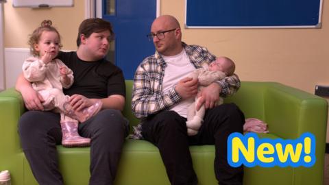Two dads with their two babies, sat on a sofa