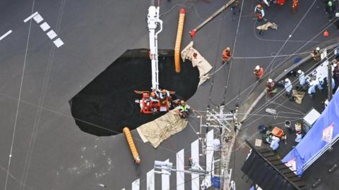 Aerial view of a sinkhole, surrounded by fire trucks and rescuers