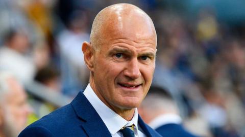Leeds Rhinos head coach Brad Arthur, dressed in blue jacket, white shirt and blue-and-yellow tie, looks into the camera.