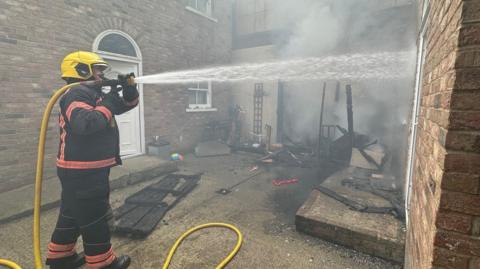 Firefighter sprays water from a hose on to a smoking building.