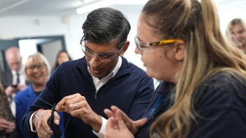 Prime Minister Rishi Sunak is shown how to splice a wire by a field service engineer apprentice