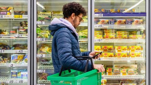 A man with a shopping basket in the freezer aisle of a supermarket