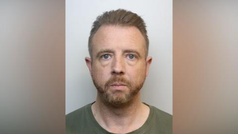 Police mugshot of Alan Styles. He is wearing a green T-shirt and he has short ginger hair and a short ginger beard. He has a nose ring.