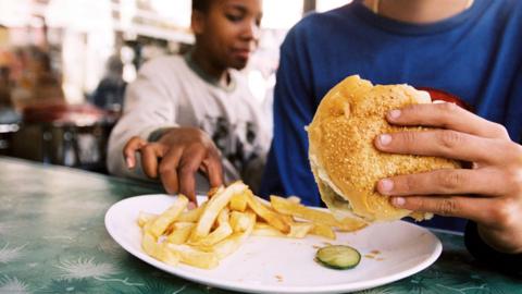 A boy reaches for another boys chips from his plate. 
