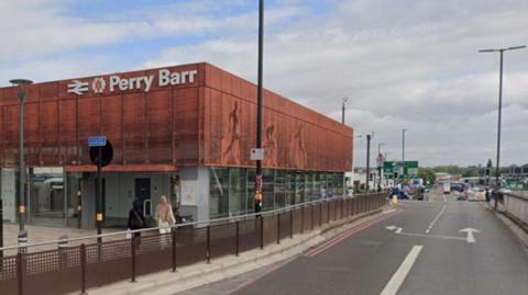 A red brick building with the words Perry Barr on the side, next to a road