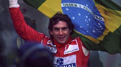 Ayrton Senna celebrates winning the European Grand Prix at Donnington in 1993, holding a Brazilian flag behind his head.