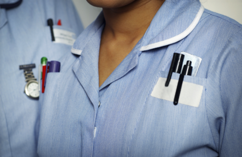 A stock image of two nurse's torsos both wearing blue uniforms with pens in breast pockets and a fob watch