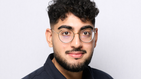 Image of Pavan Bhatt, a man with short dark curly hair and glasses wearing a black shirt and standing in front of a white background