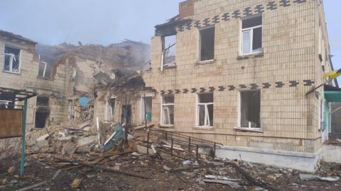 The aftermath of an air strike on a hospital in Sumy. Smoke can be seen rising from the caved-in wing.