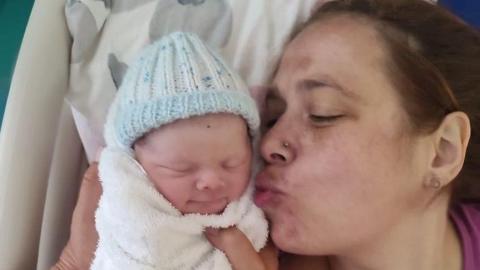 Women laying down on a hospital bed kissing her newborn baby wrapped in a towel