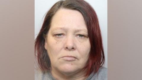 A police-issued mugshot of Jayne Hill, who has long, dyed red hair and stares impassively at the camera.