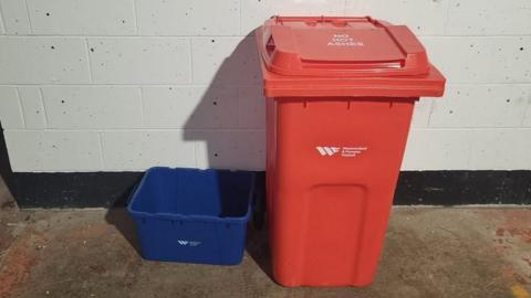 Red large waste bin next to small blue recycling bin