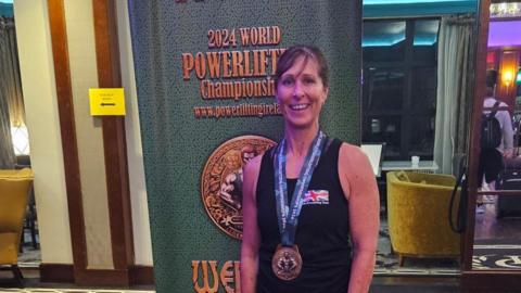 Louise Clark smiling at the camera in a black tank top with a gold medal around her neck.