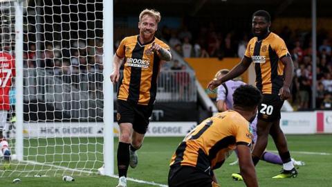 James Brophy runs away smiling and pointing at Elias Kachunga, who set up his opening goal for Cambridge United against Charlton Athletic