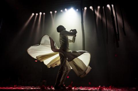 A man dances on stage at The Mount Without in Bristol. He is wearing a white outfit and is illuminated by multiple spotlights