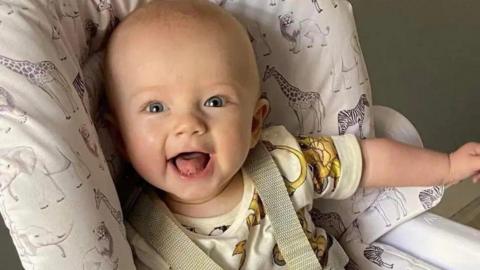 A baby boy smiles widely in a high chair