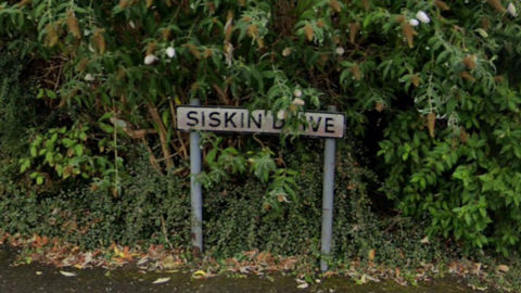 Sign which reads Siskin Drive in front of a bush