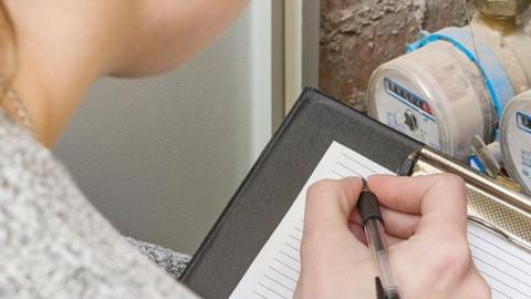 A woman about to write notes on a clipboard as she takes a reading from a water metre