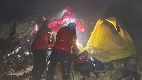 People in red coats have set up a yellow tent in the dark in heavy rain
