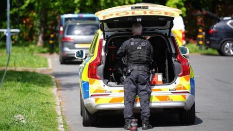 Kenton synagogue attack, image shows police officer stood behind a police car on a leafy street