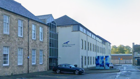 A street view of the white concrete East Lothian Council headquarters with their blue logo on the side.
