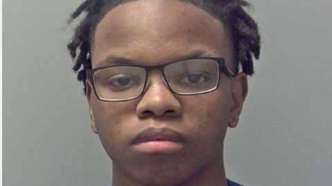 A custody photo of an expressionless teenager with black-framed glasses, brown eyes and black hair 