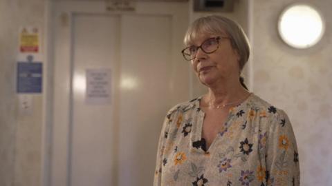 Hilary Jonathan, a woman with a grey ponytail and wearing glasses, stood in front of the broken lift.