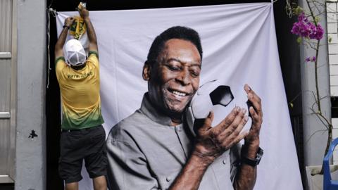 A fan in a Brazil shirt hangs up a large banner of Pele holding a football