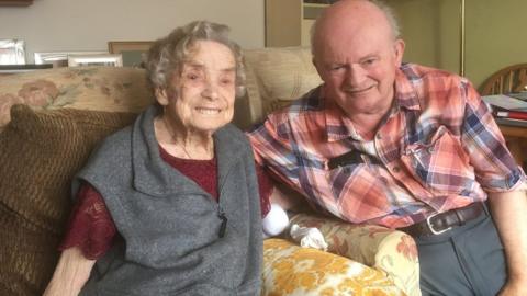 Norah Witkiss and Malcolm Yates sitting on their sofa at home