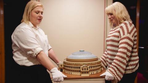 Two women carry a model of the Royal Albert Hall